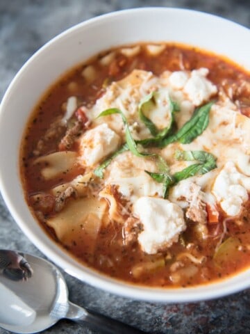 a white bowl filled with lasagna soup and topped with cheese