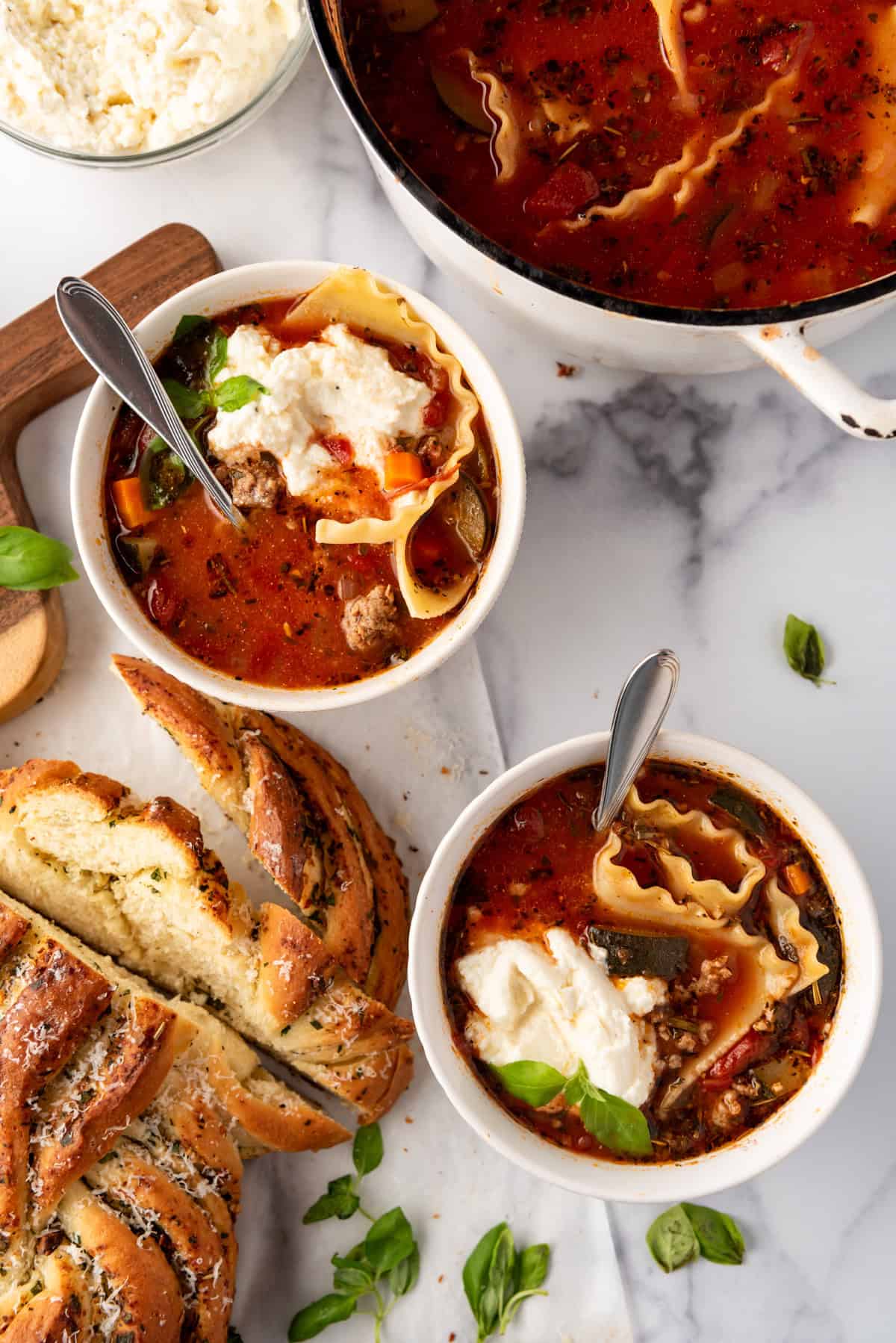 Two bowls of lasagna soup next to a loaf of garlic bread.