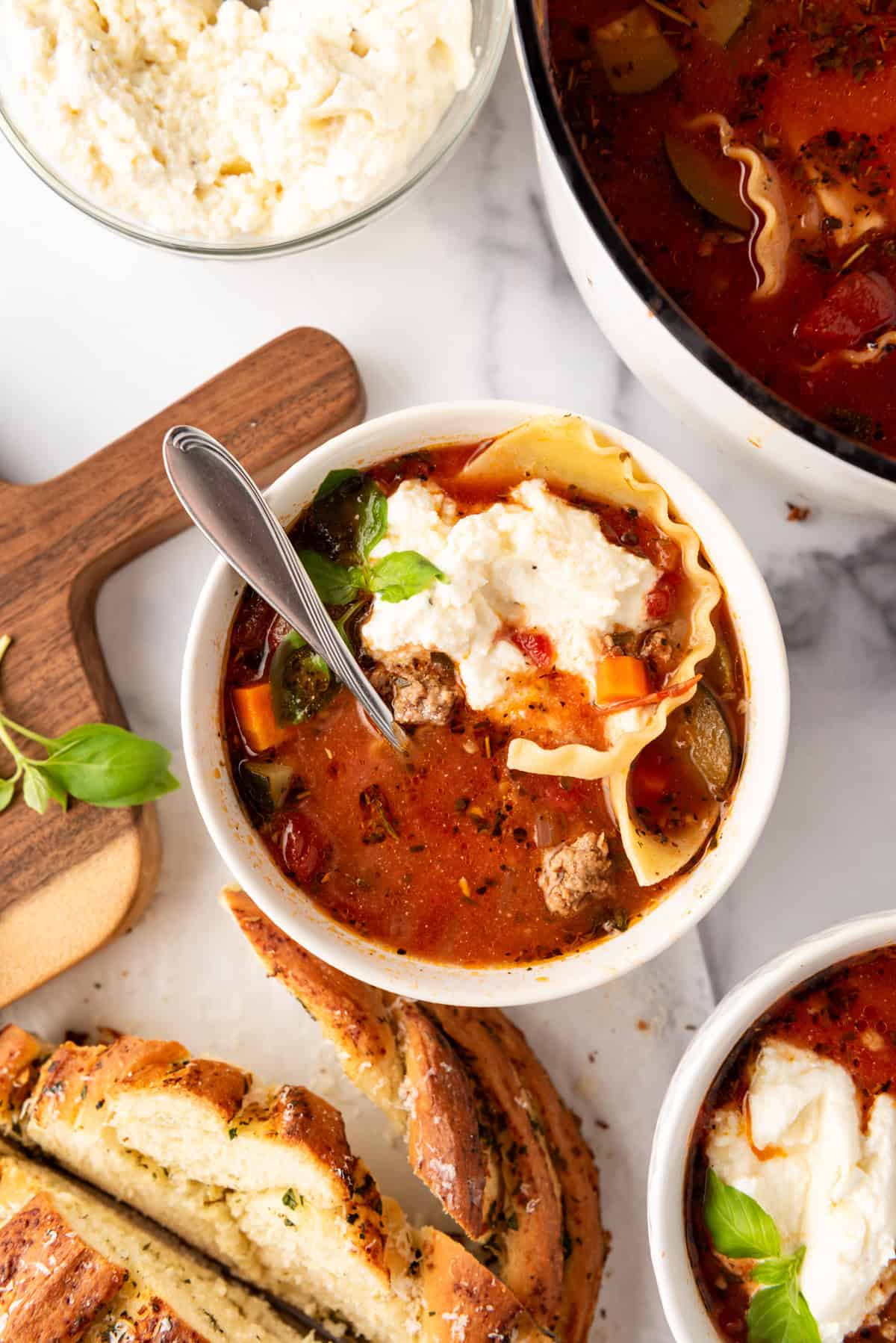 An overhead image of a bowl of lasagna soup next to garlic bread.