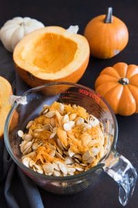 a large glass measuring cup full of pumpkin guts next to a sliced pumpkin halve and some orange and white whole pumpkins