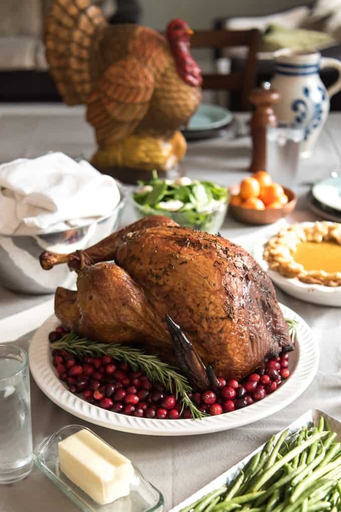 a smoked turkey on a white plate surrounded by cranberries with a turkey statue in back and other food dishes around it