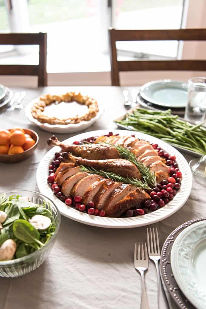 sliced turkey with two legs in the center on a white plate surrounded by cranberries and topped with fresh rosemary
