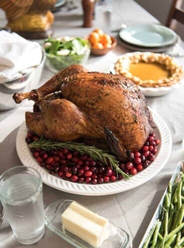 a whole smoked and brined turkey on a white plate with whole cranberries and surrounded by other food dishes