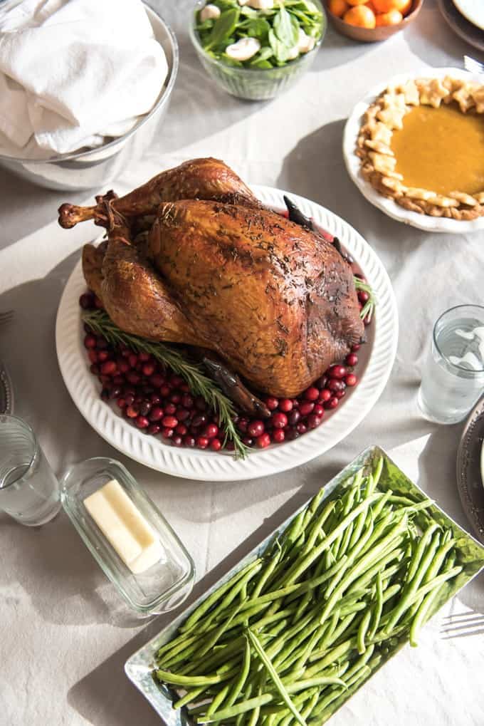 a smoked turkey on a white plate surrounded by cranberries with a salad pumpkin piegreen beans and butter all placed around the table