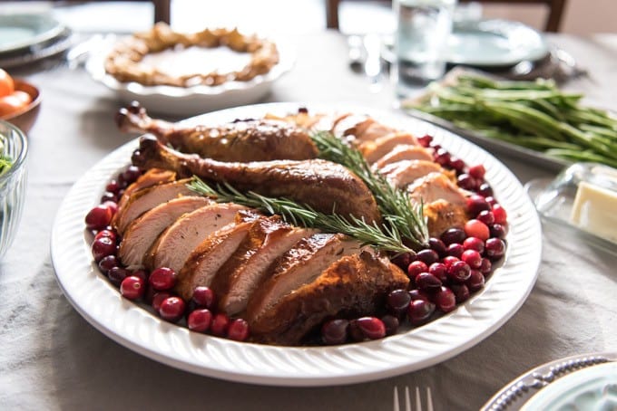 in the center of the image is a white plate with cranberries around a sliced turkey and rosemary sprigs