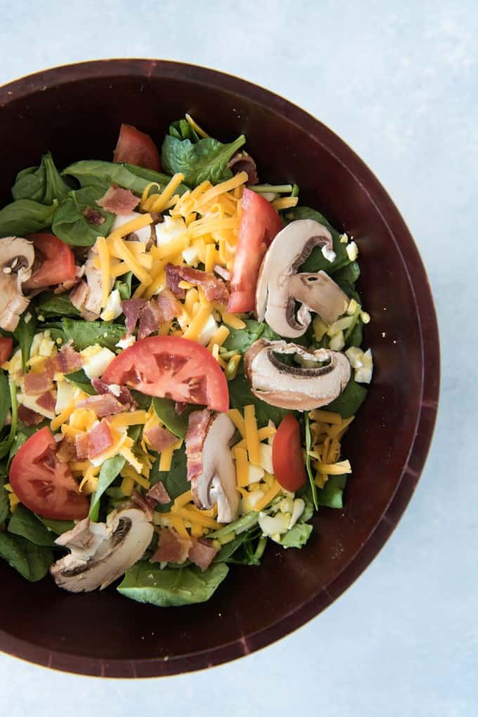 a bowl of spinach salad with sliced mushrooms, tomatoes, cheese and more