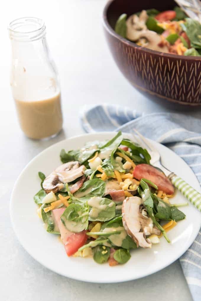 a white plate filled with salad net to a bottle of dressing and a bowl of ore salad off to the side