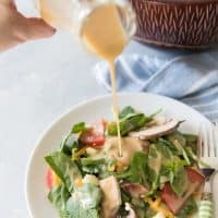 pouring honey mustard dressing onto a green salad