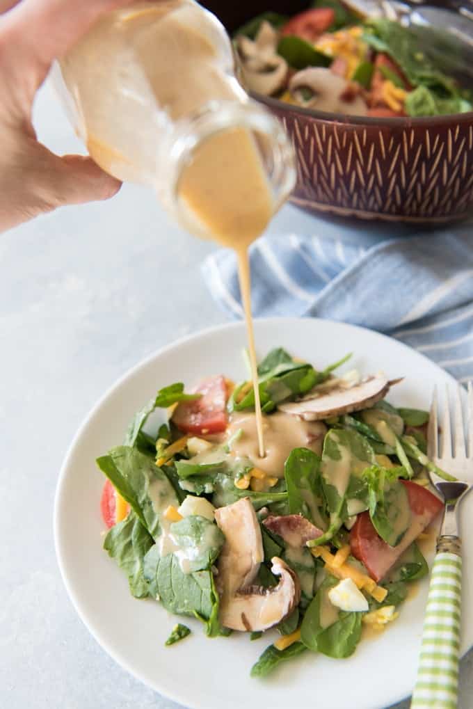 pouring honey mustard dressing onto a green salad