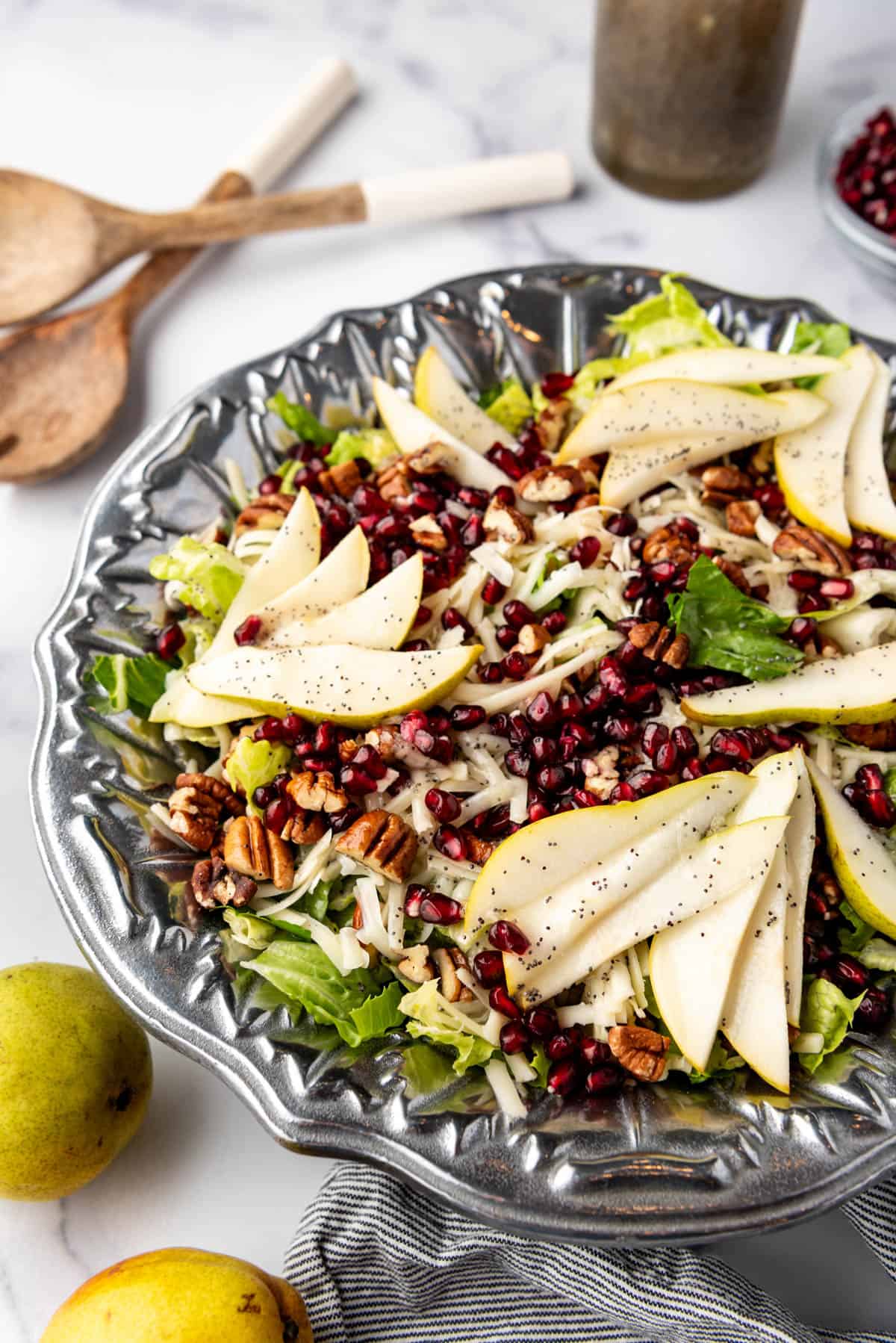 A side view of a salad with sliced pears, pomegranates, pecans, and swiss cheese.