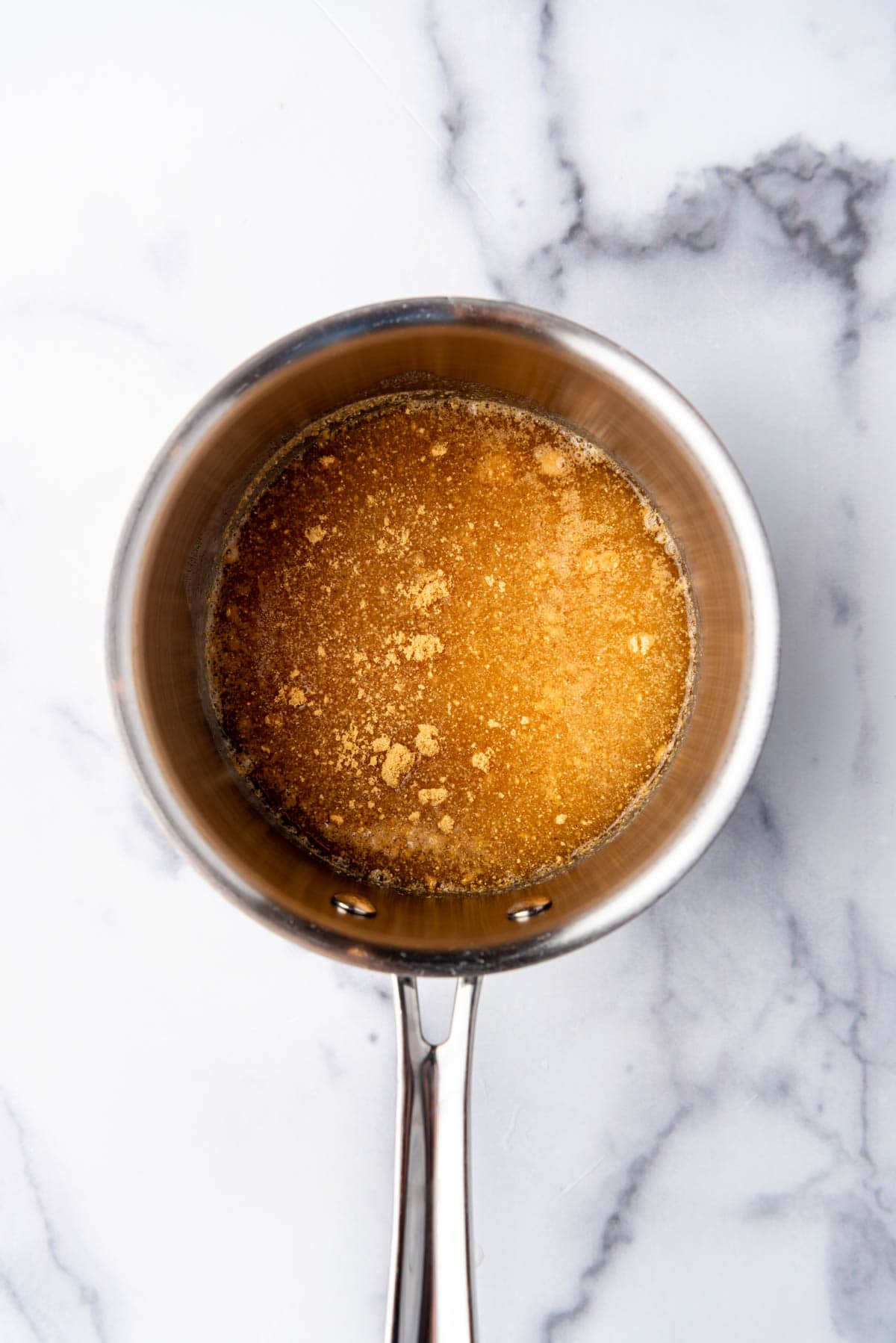 Adding sugar, vinegar, and oil to a saucepan.