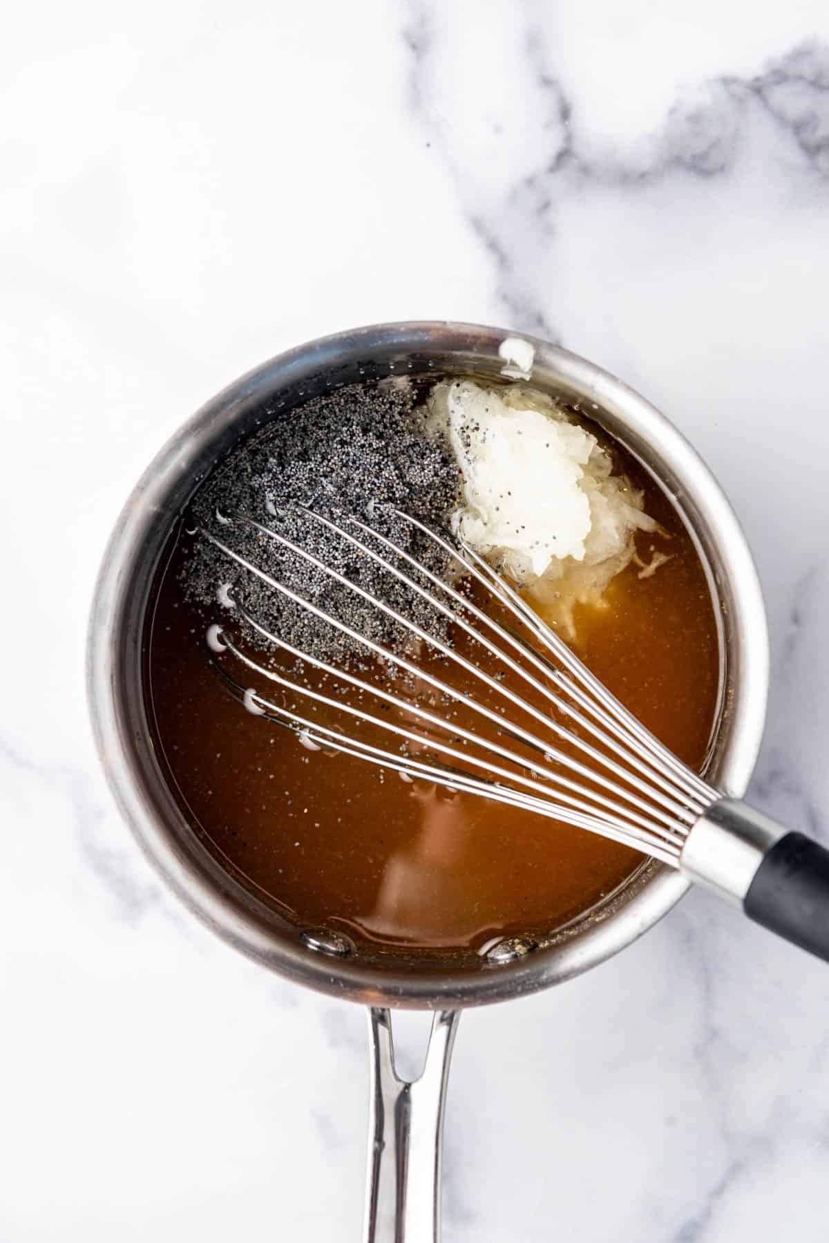 Adding poppy seeds and grated onion to salad dressing in a saucepan with a whisk.