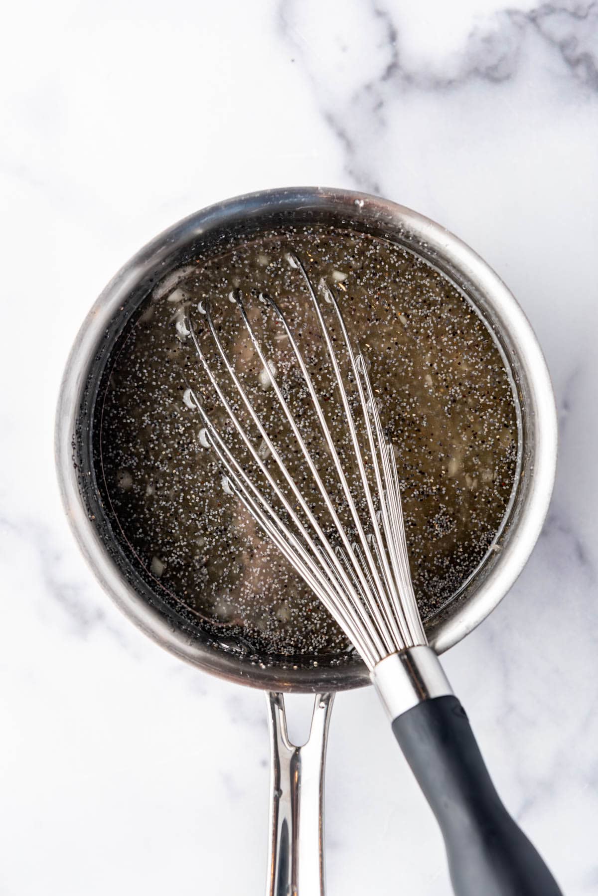 Poppy seed salad dressing in a saucepan with a whisk.