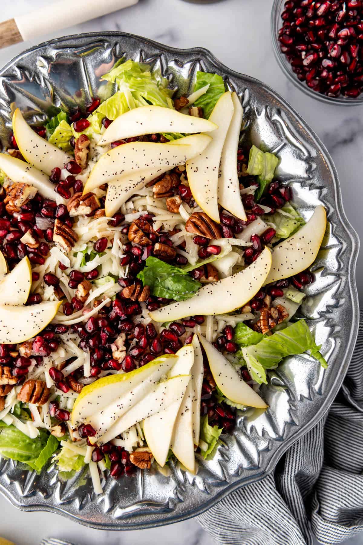 A close overhead image of a salad topped with sliced pears and pomegranates with poppy seed dressing.