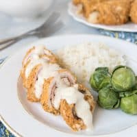Chicken Cordon Bleu sliced and covered in sauce ona white plate next to brussel sprouts