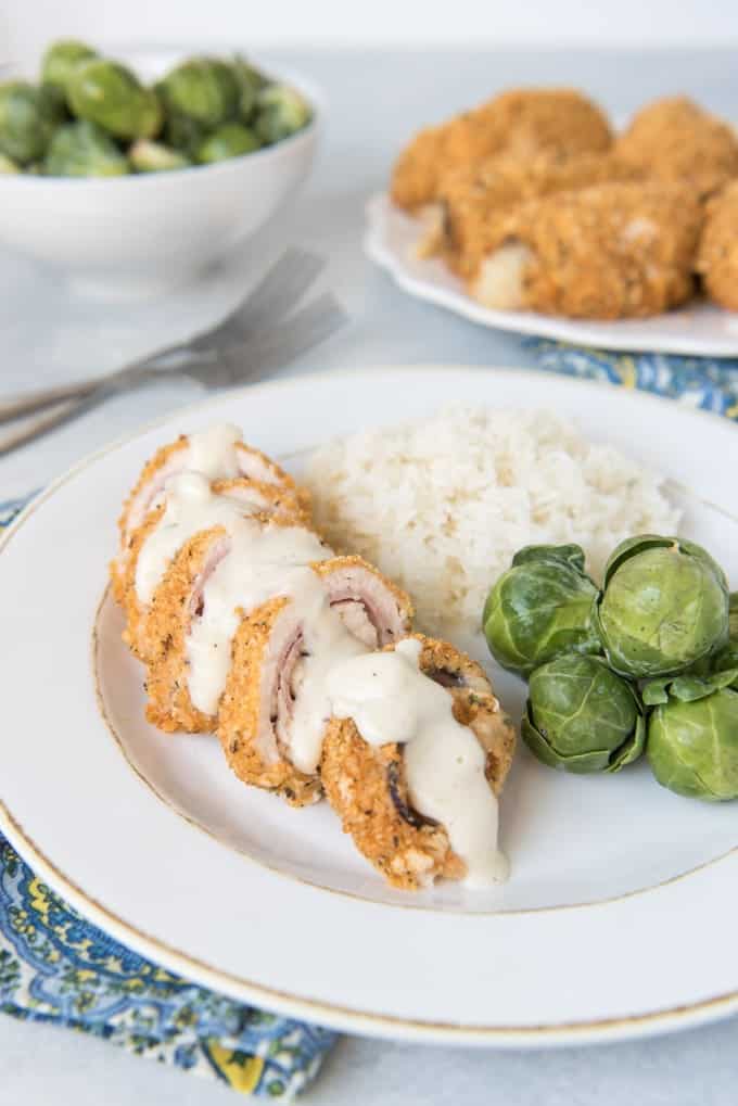 Chicken Cordon Bleu sliced and covered in sauce on a white plate next to brussel sprouts