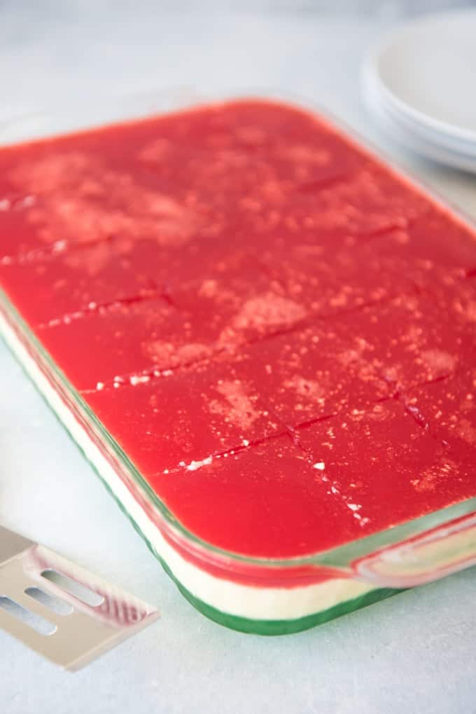 a glass baking dish with layered green white and red jello inside and cut into squares