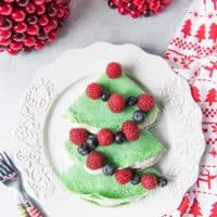 christmas tree shaped crepes on a plate with whipped cream and berries as garland