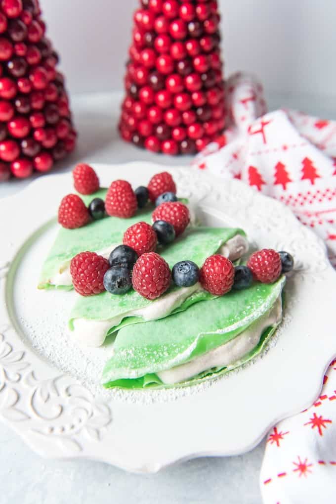 Christmas Tree Crepes with Gingerbread Spice Whipped Cream on a white plate with fresh berries