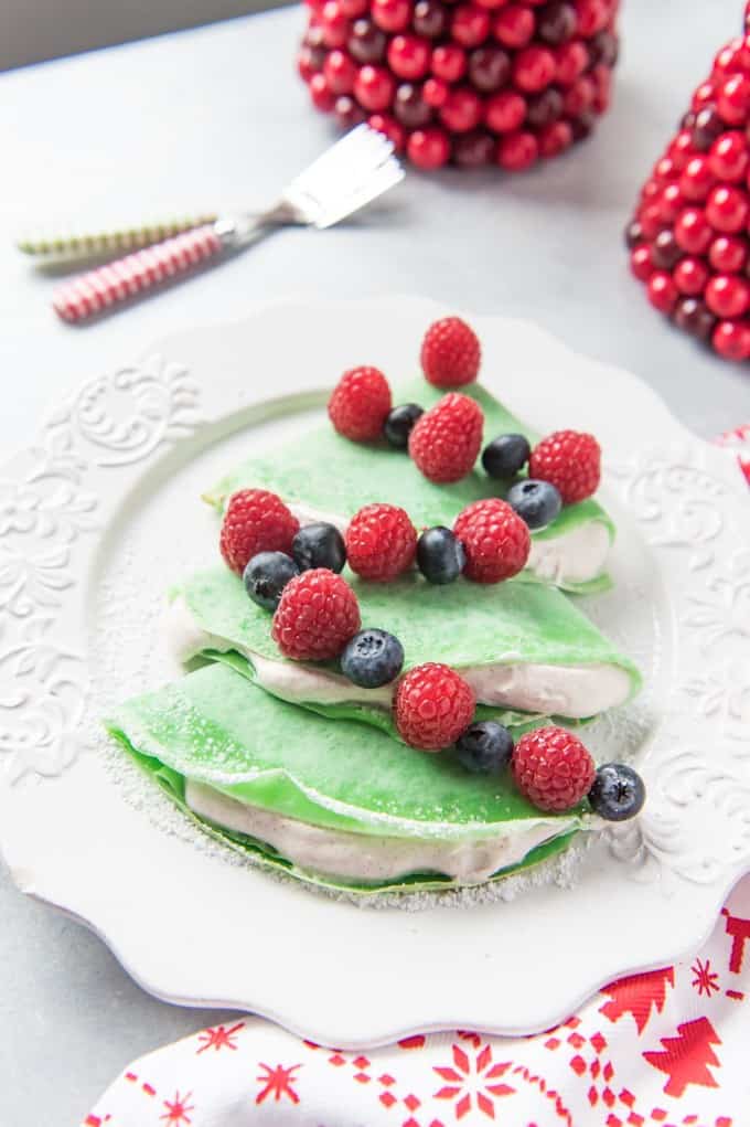 a white plate with green christmas tree crepes and a berry garland