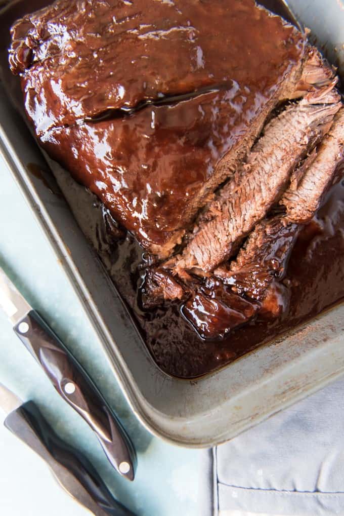 a slow roasted bbq brisket sliced and in a baking dish next to knives