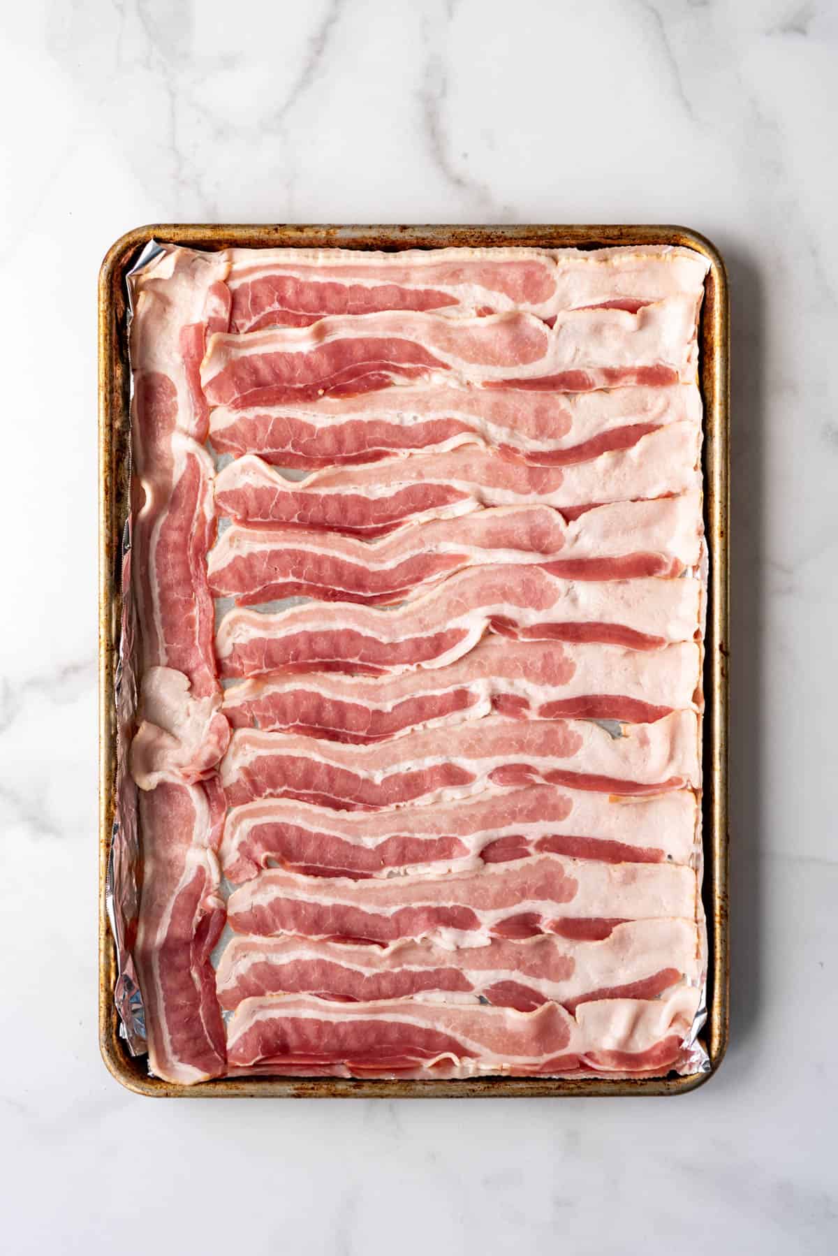 Slices of raw, uncooked bacon on a baking sheet.