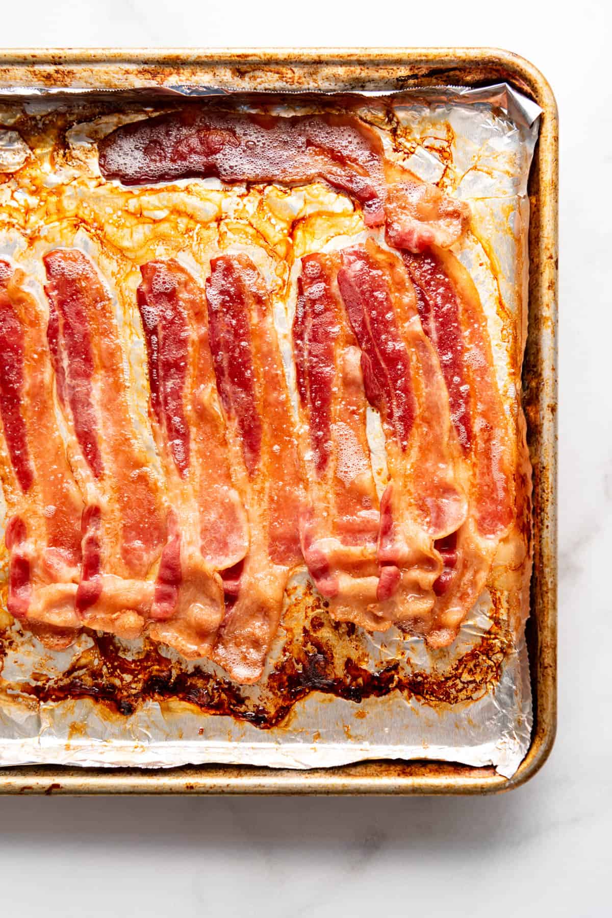 Cooked bacon in bacon grease on a baking sheet.