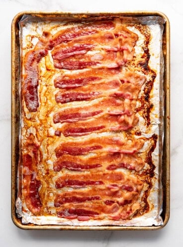 A pound of cooked bacon on a baking sheet.