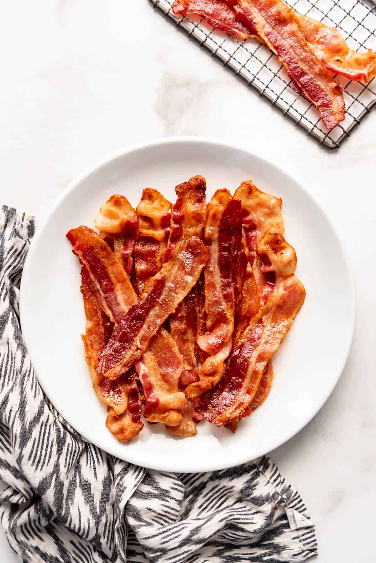 Slices of crispy bacon on a white plate beside a cloth napkin.