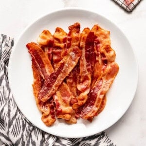 Slices of crispy bacon on a white plate beside a cloth napkin.