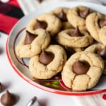 A plate filled with peanut butter blossom cookies with a few scattered hershey kisses around it.