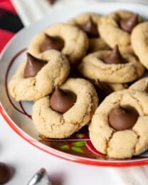 A plate filled with peanut butter blossom cookies with a few scattered hershey kisses around it.