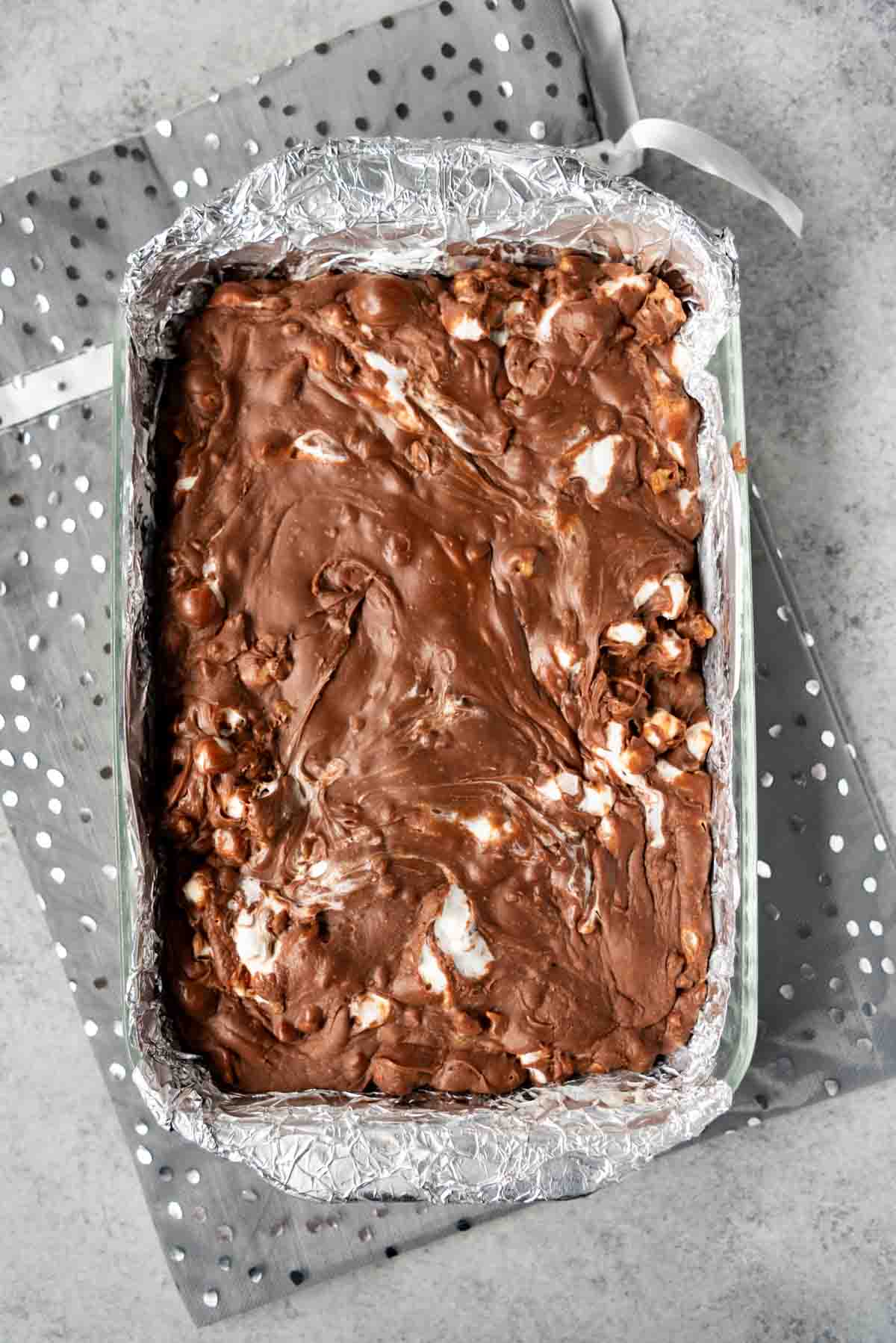 Foil lined baking dish with rocky road fudge inside and a sparkly dotted gray bag underneath.