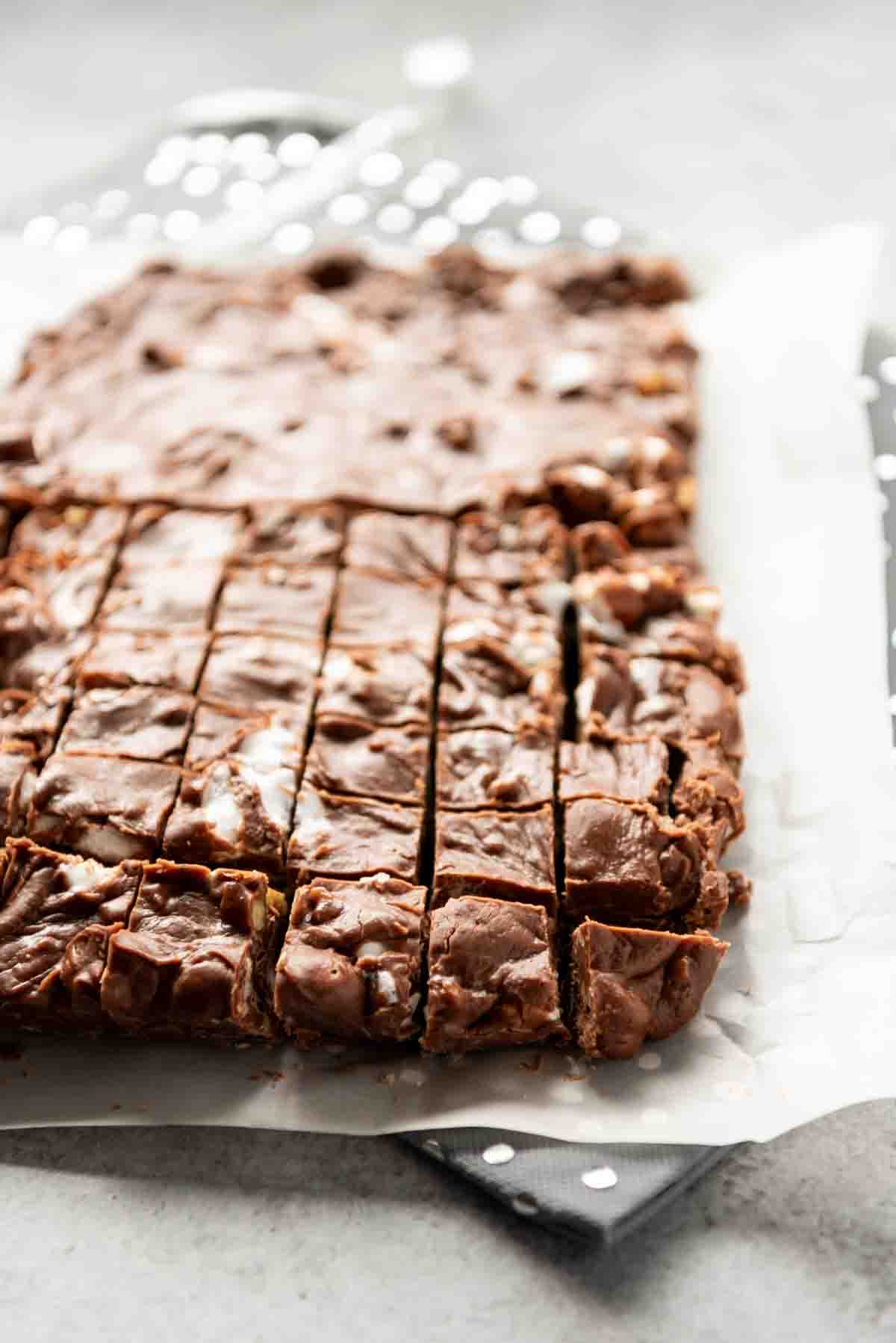 A side view of rocky road fudge cut into small squares for serving and resting on a piece of parchment paper.