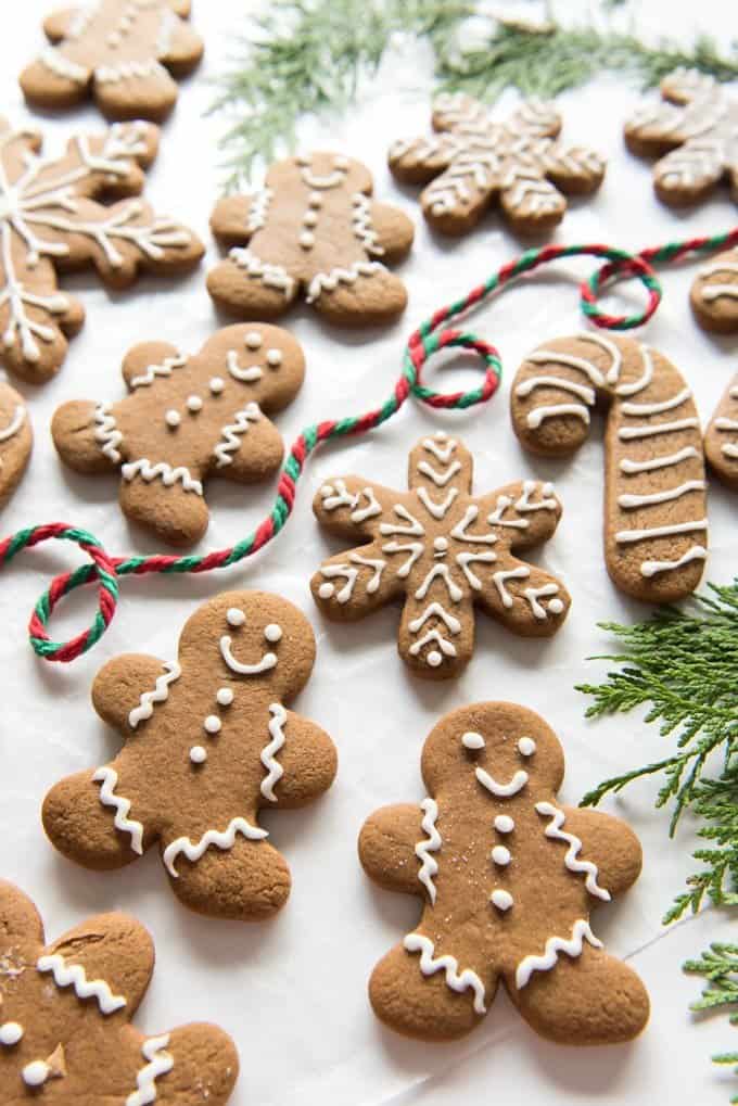 gingerbread cookie shapes decorated in white icing with tirling loops of yarn and green sprigs around them