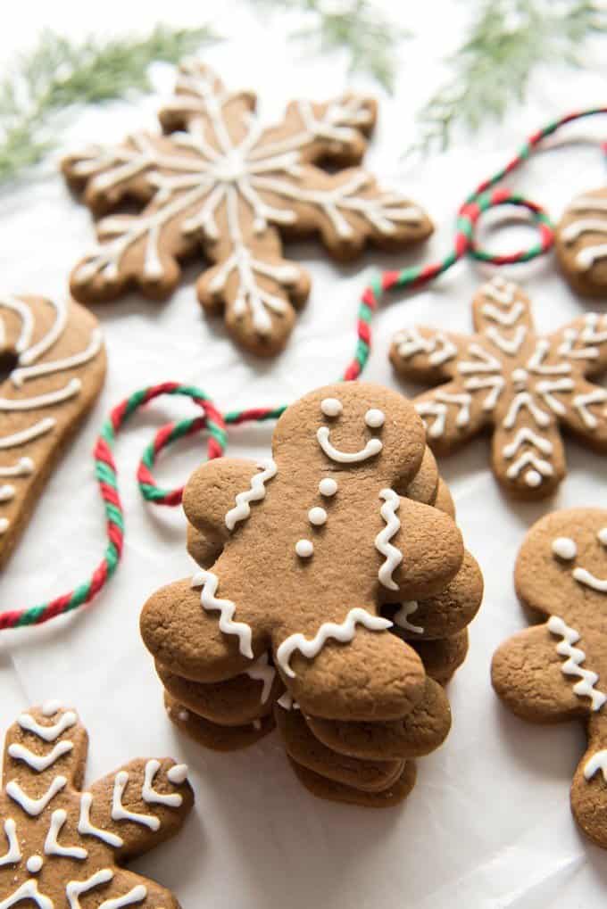 stacked gingerbread men surrounded by other gingerbread cookies and a piece of striped yarn behind them. green tree sprigs at the top of the image