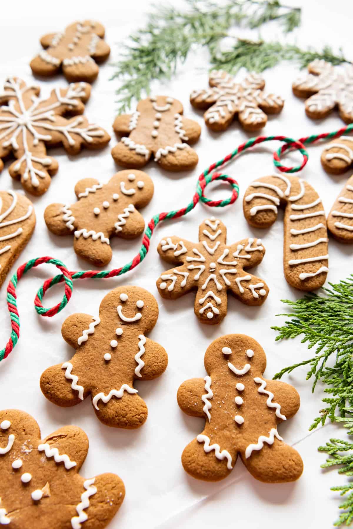 Gingerbread cookie shapes decorated in white icing with twirling loops of yarn and green sprigs around them.