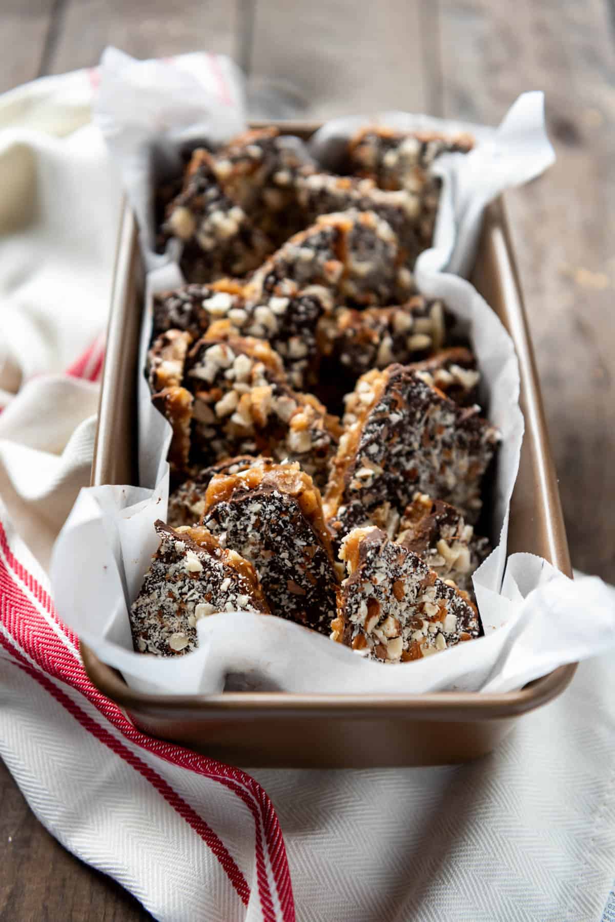 a bread pan filled with english toffee pieces on a red and white striped towel