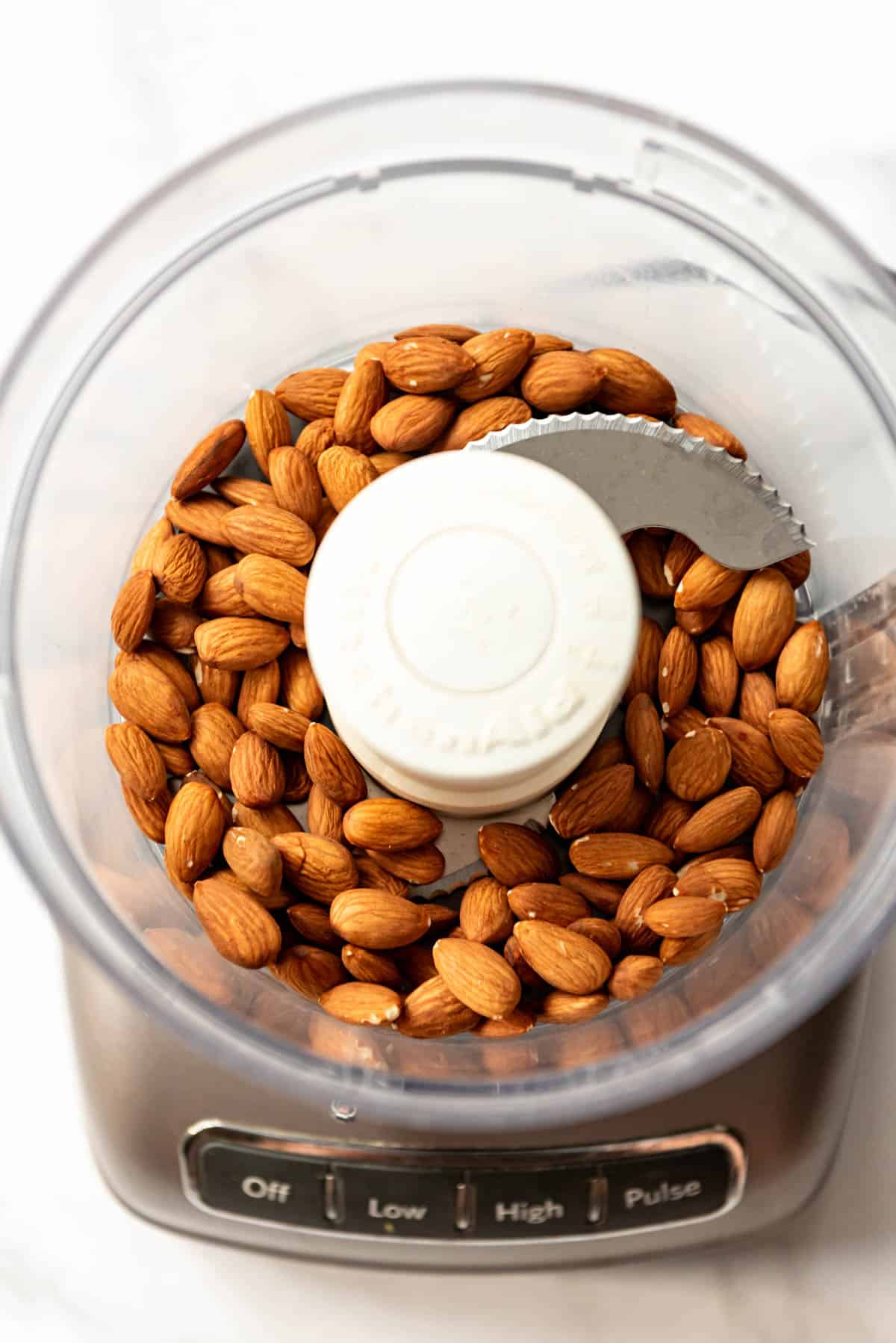 An overhead image of whole toasted almonds in a food processor.