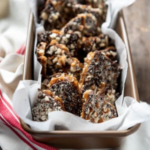 a bread pan filled with english toffee pieces on a red and white striped towel