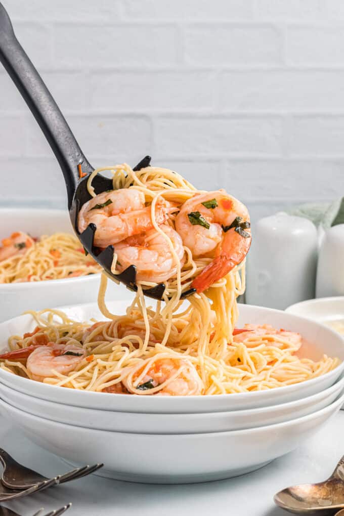 A serving spoon lifting a bunch of pasta and shrimp from a serving bowl.