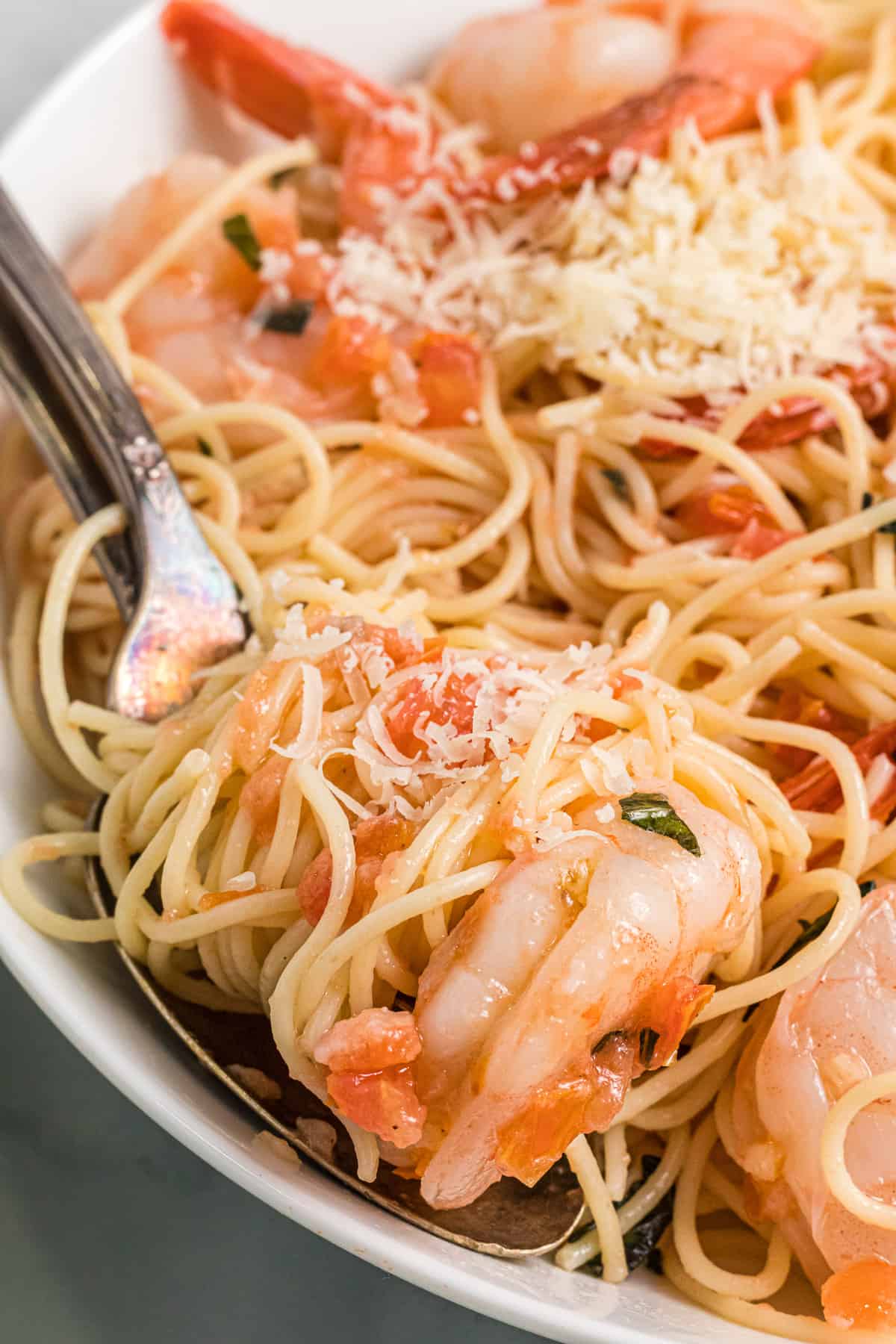 Angel hair pasta on a fork with shrimp and tomatoes.