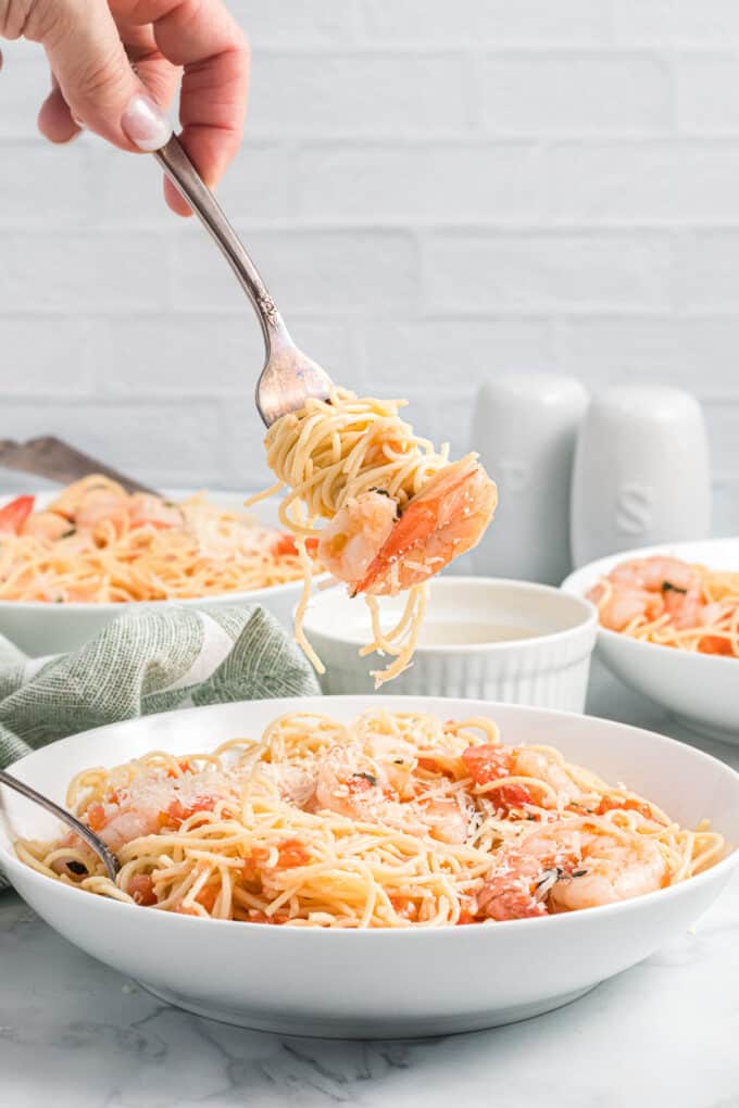 A fork holding swirled pasta and shrimp over a bowl.