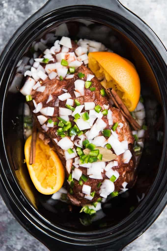 a slow cooker with the ingredients for crispy slow cooked pork carnitas inside