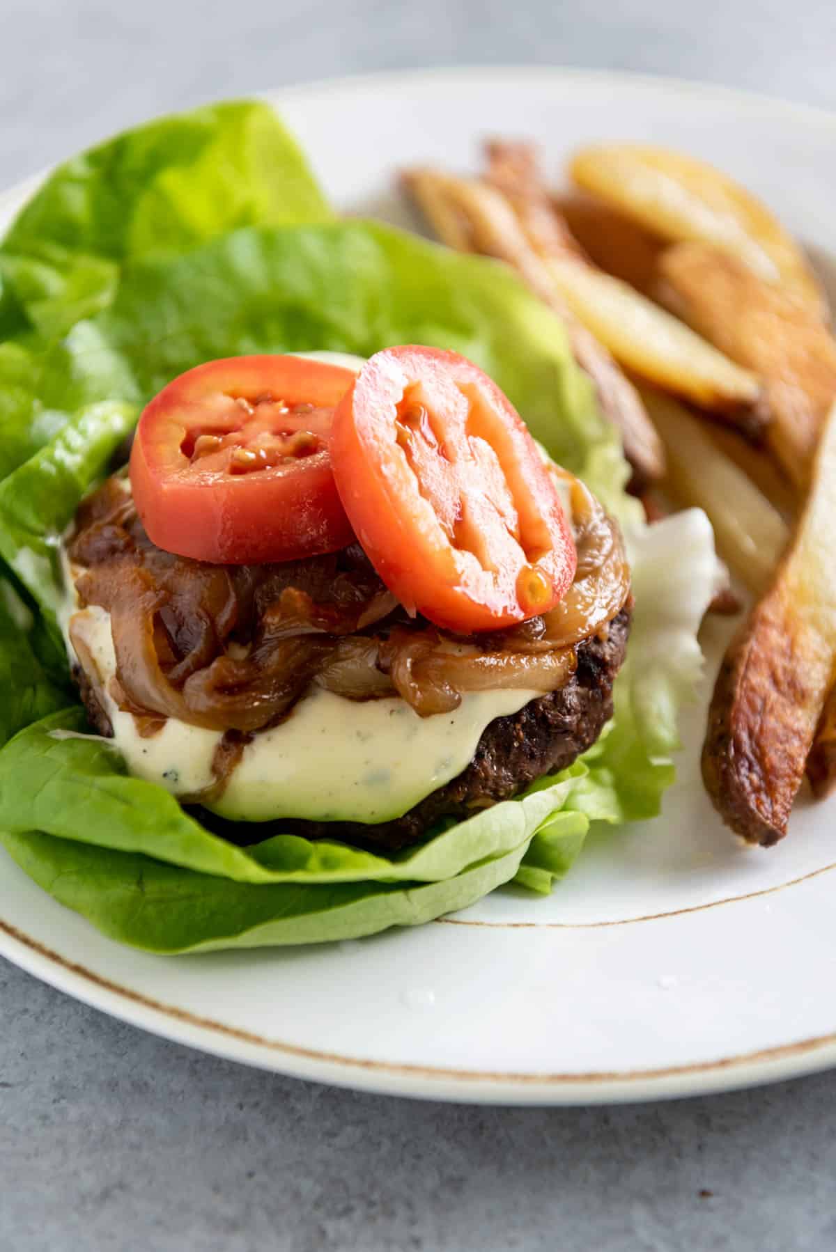 A burger and fries on a plate and the burger is topped with aioli as an example of how you can use it.