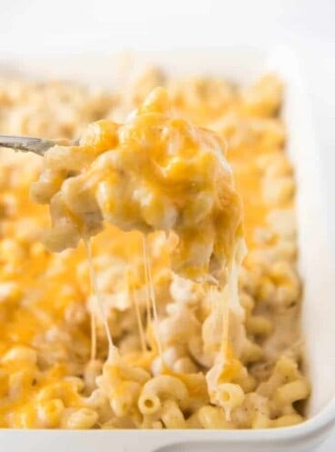 a spoon holding up a creamy cheesy scoop of mac and cheese above a baking dish