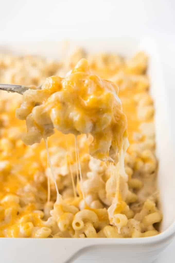 a spoon holding up a creamy cheesy scoop of mac and cheese above a baking dish