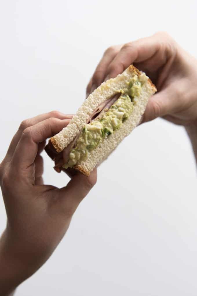 two hands holding up a green eggs and ham sandwich