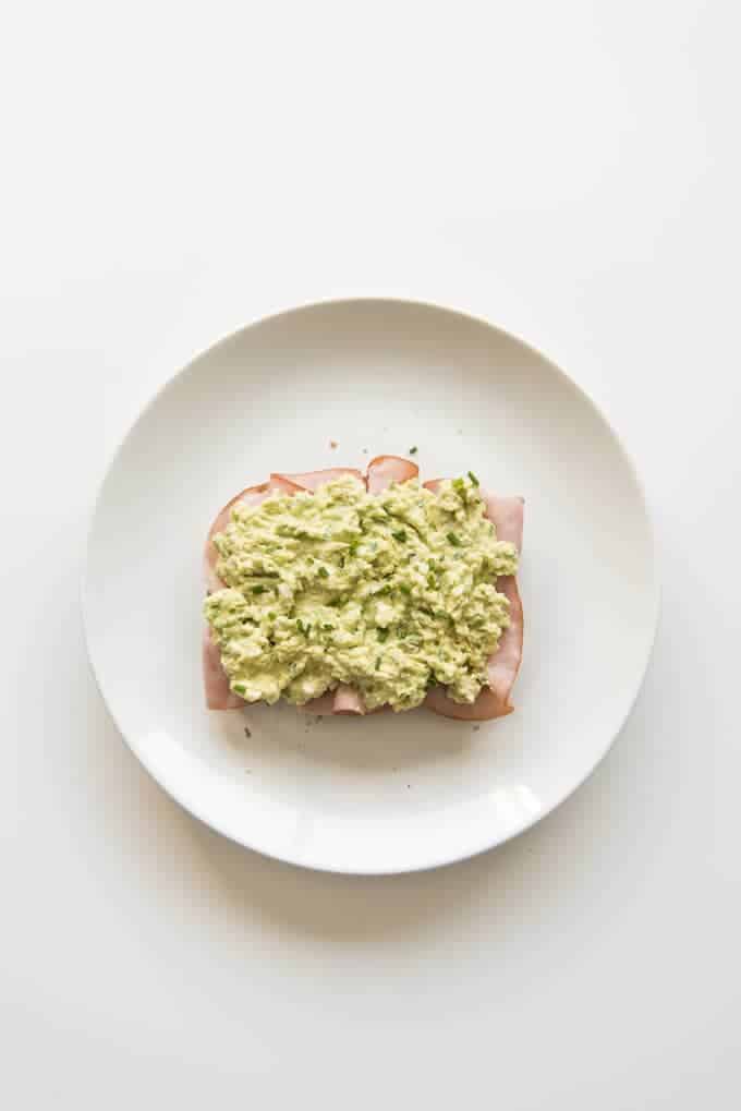 green egg salad topped ham on an open sandwich on a white plate