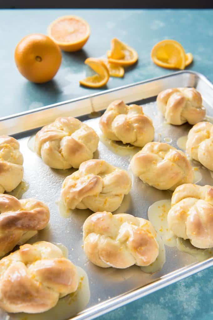 a baking sheet with knotted sweet rolls and orange slices in the background